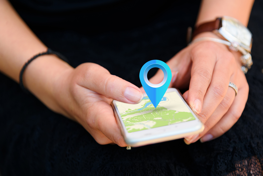 Woman holds a smartphone which shows a location on a map